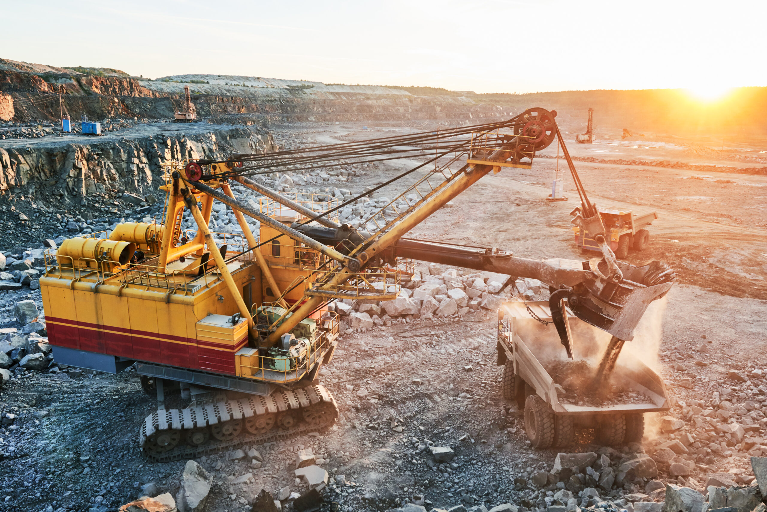 Mining industry. Heavy excavator loading granite rock or iron ore into the huge dump truck at opencast quarry. Sunset